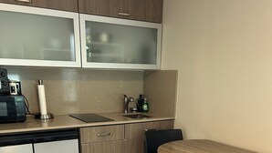 Cocina compacta con microondas, pileta y alacenas. Se aprecia una mesa redonda con sillas y un bote de basura.