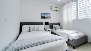 A bedroom with two beds, a wall-mounted air conditioner, and a window with blinds. - Dream House on Isla Verde Beach + Terrace (Carolina)