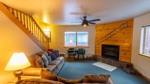 A cozy living room with a wooden staircase, a fireplace, and a comfortable seating area. - Cabins at Strawberry - Fir (Strawberry)