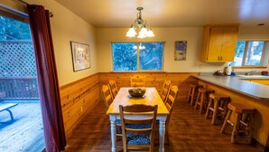 A wooden dining table with chairs, a wooden bench, a kitchen counter with stools, and a window with a view of trees. - Cabins at Strawberry - Fir (Strawberry)