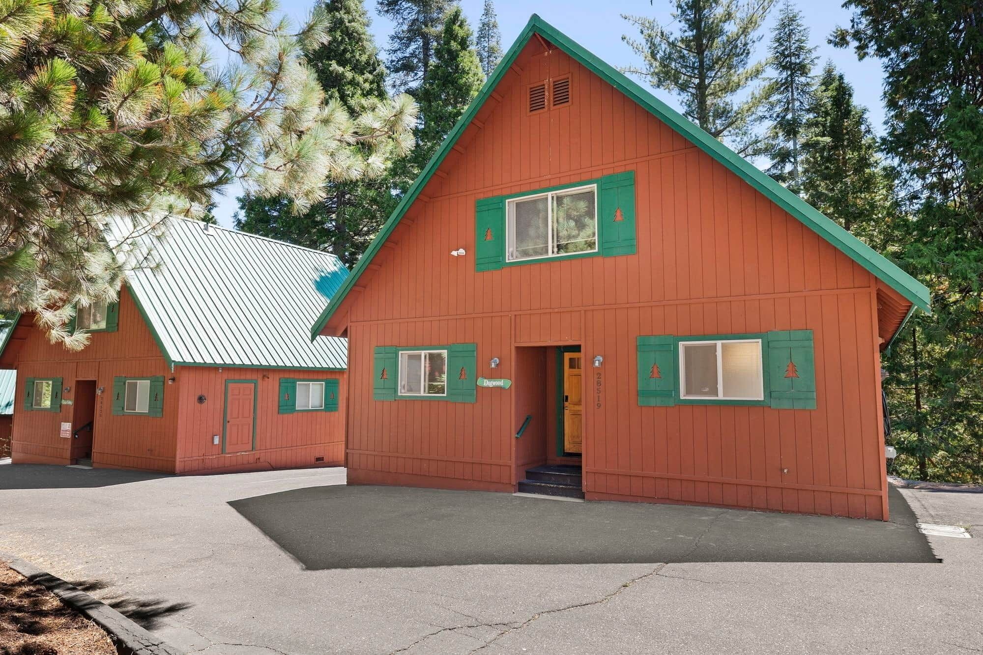 A red wooden cabin with green shutters, a metal roof, and a concrete driveway.