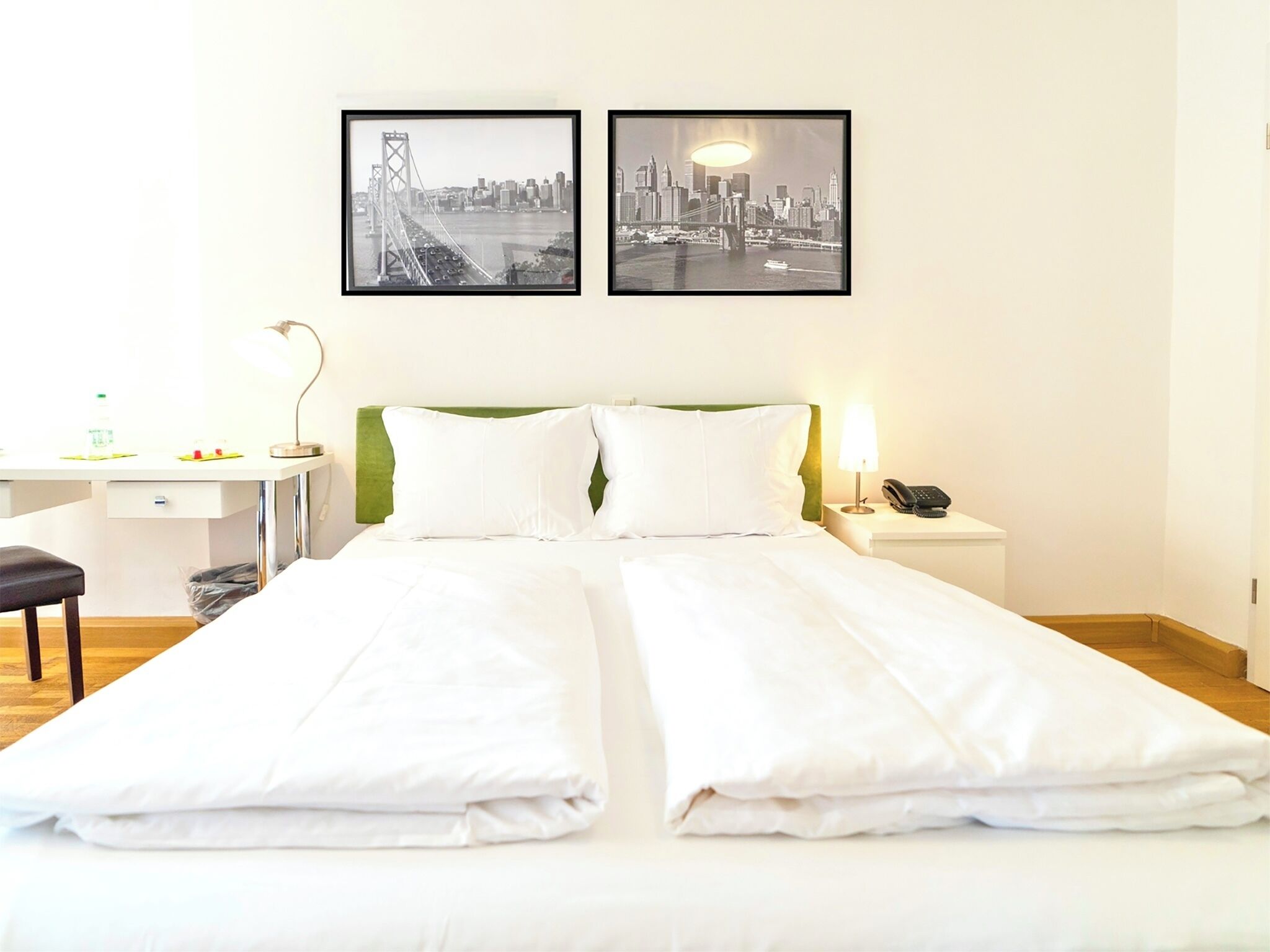 Ein Hotelzimmer mit einem Bett, einem Schreibtisch, einem Sessel, einem Telefon und zwei gerahmten Bildern an der Wand.