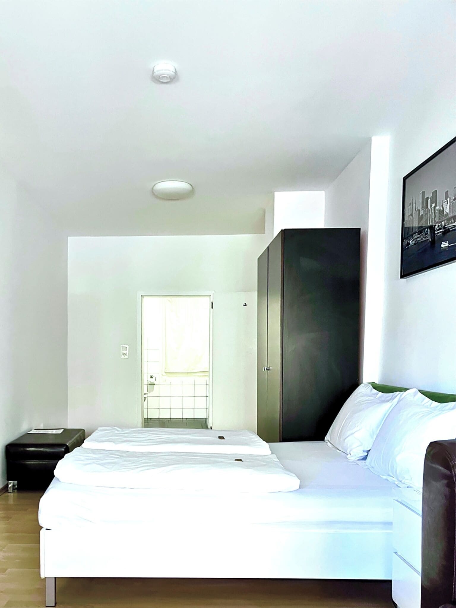 A bedroom with a bed, a wardrobe, a door leading to a bathroom, and a framed picture on the wall.