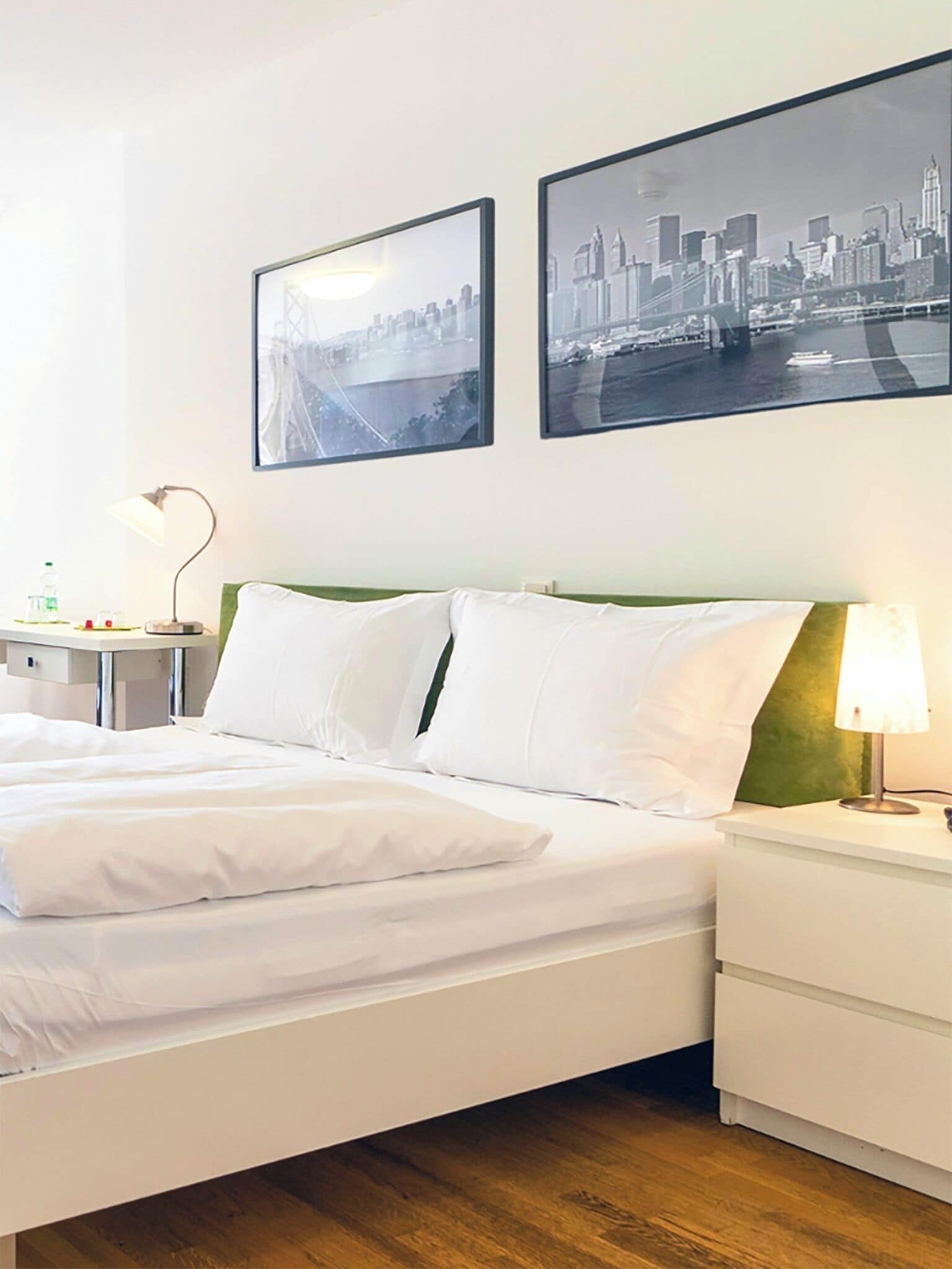 Ein Hotelzimmer mit einem Bett, Nachttischen, einer Lampe und zwei gerahmten Bildern an der Wand.