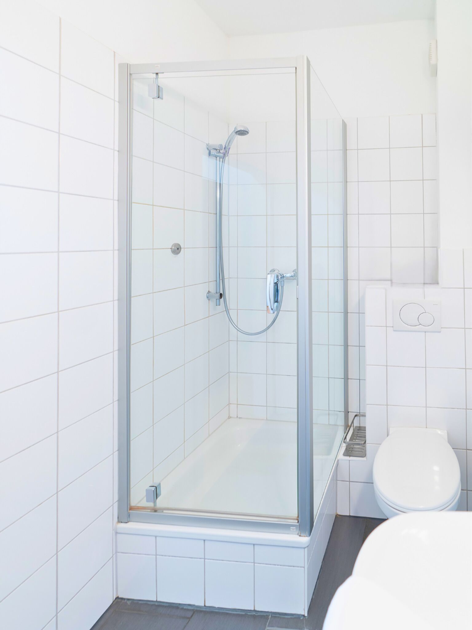 A glass-enclosed shower stall with a handheld showerhead and a wall-mounted faucet.