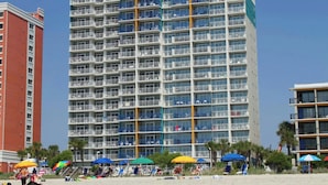 A multi-story hotel with balconies, located near a beach with umbrellas. - Atlantica III PH64- Oceanfront 1BR- Lazy River (Myrtle Beach)