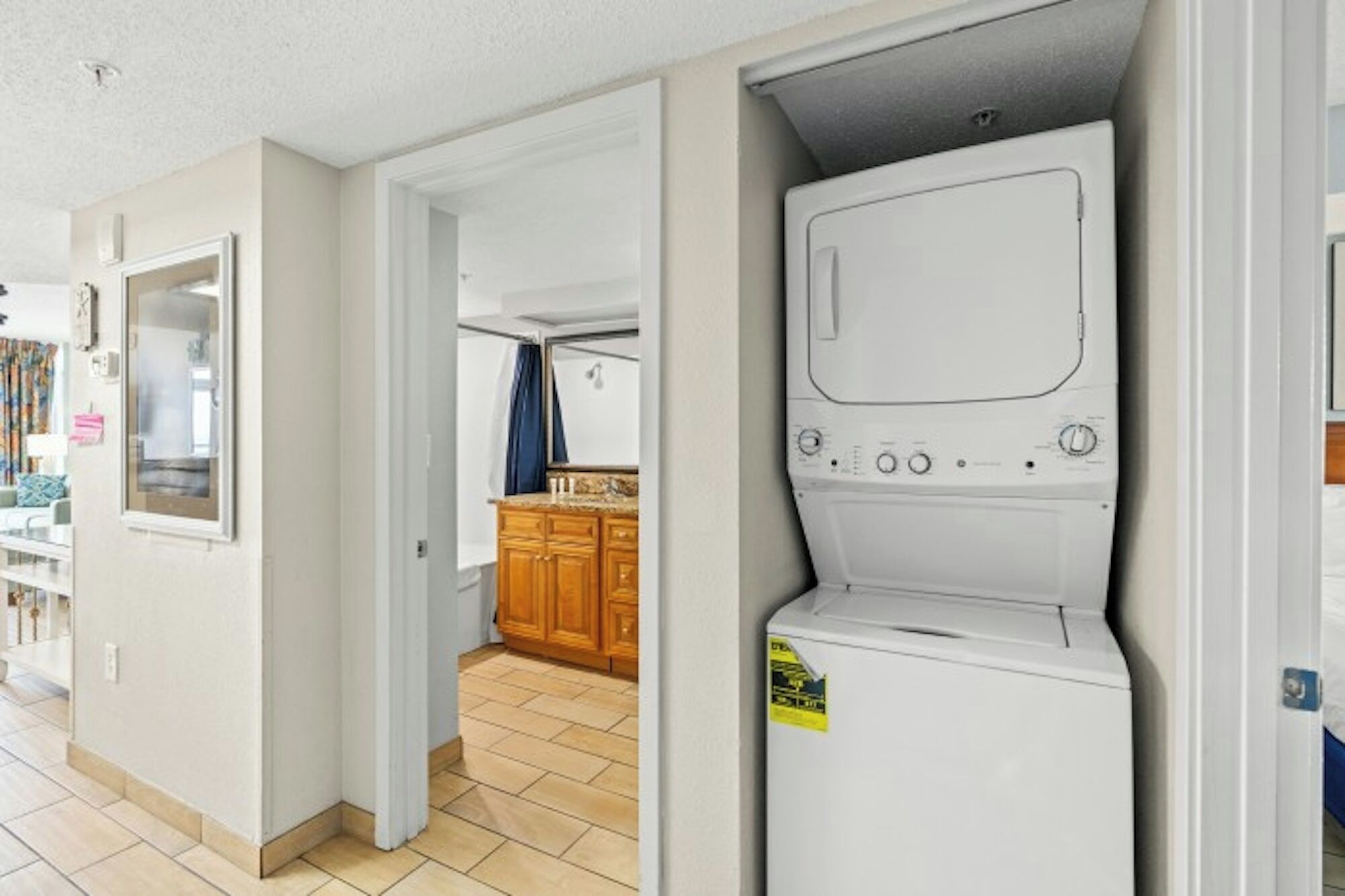 A laundry room with a washing machine and dryer, a wooden cabinet, and a bathroom with a mirror and towel rack.