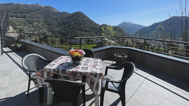 A terrace with a table set for two, a potted plant, and a view of a mountainous landscape.
