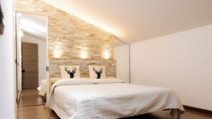 A bedroom with a bed, a wooden door, a stone wall, and two wall-mounted lights.