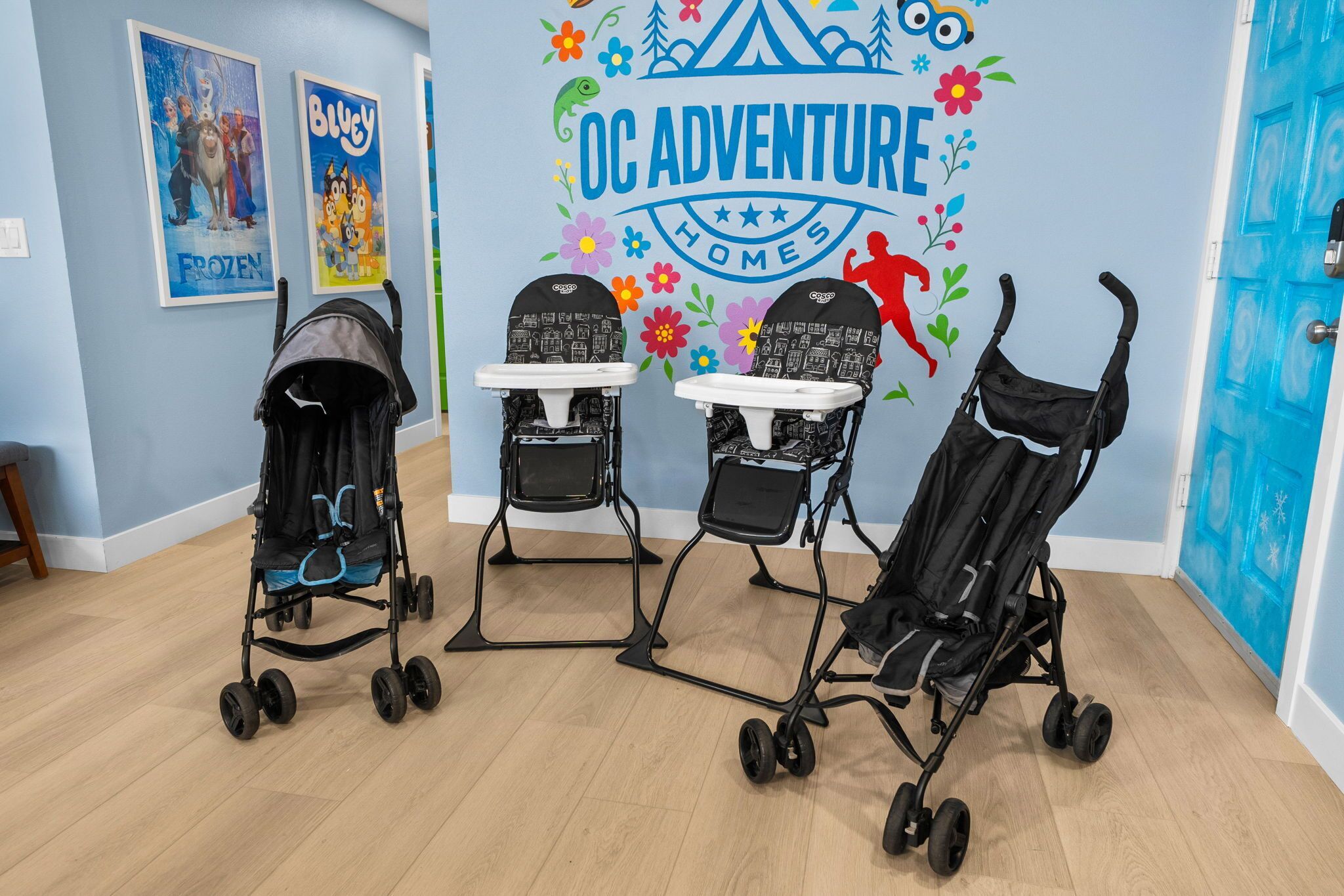 Ein Zimmer mit drei Kinderwagen vor einer Wand mit dem Schild 'OC ADVENTURE HOMES' und Filmplakaten.