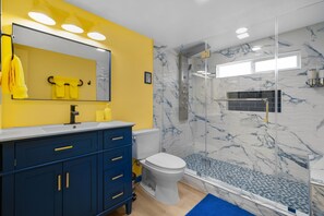 A bathroom with a yellow wall, a marble shower, and a white toilet. - Enchanted Dreams: Theater, Arcades, Playground + (Garden Grove)