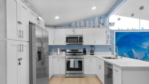 A modern kitchen with white cabinets, stainless steel appliances, and a blue accent wall.