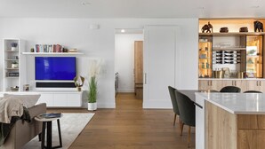 A modern living room with a flat-screen TV, a bookshelf, and a dining area with a wooden island. - Welcome to Lucky 13 • Luxurious, private escape on Lake Hills Golf Course. (Billings)