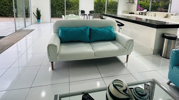 A modern living room with a white sofa, a glass coffee table, and a kitchen area with a black countertop and stainless steel appliances. - Kai Guana House (Provincia de Guanacaste)