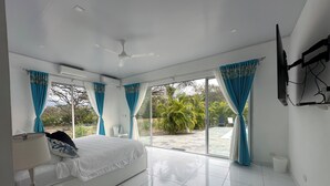 A modern bedroom with a large bed, a ceiling fan, and a TV mounted on the wall. - Kai Guana House (Provincia de Guanacaste)