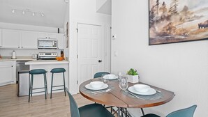 Une cuisine moderne avec des armoires blanches, un four encastré et un coin repas doté d’une table en bois, mise pour quatre personnes.
