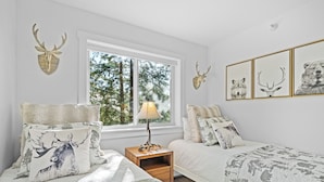 Une chambre avec deux lits, une fenêtre donnant sur la forêt et des bois de cerf accrochés au mur.
