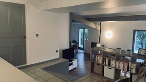 A modern living room with a flat-screen TV, a bookshelf, and a dining area with a table and chairs.