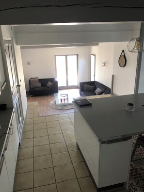 A modern kitchen with a central island, a dining area with a round table, and a living room with two sofas.