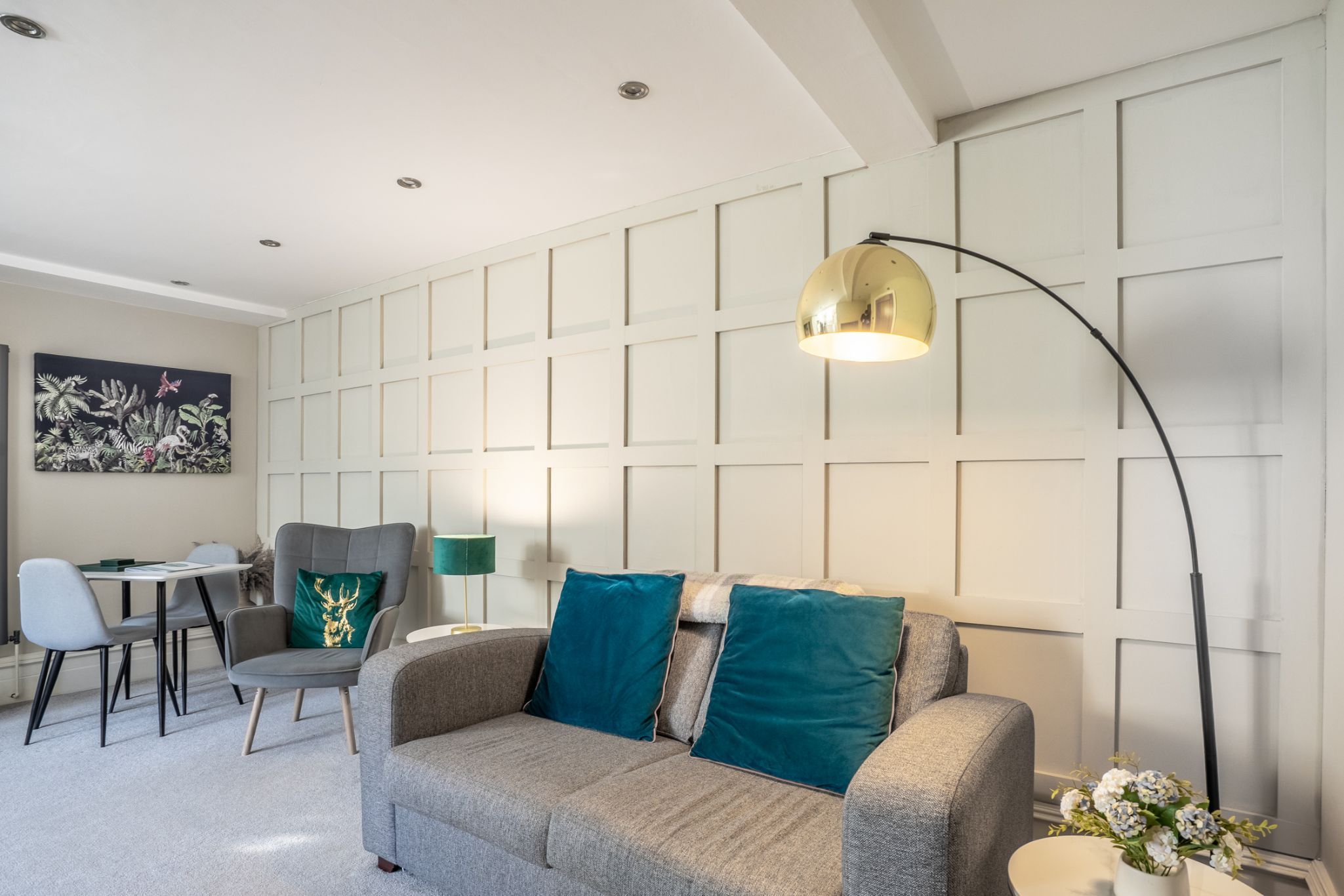 A modern living room with a grey sofa, teal cushions, a green lamp, and a painting on the wall.