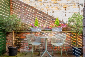A brick wall with two metal chairs and a table in the center, surrounded by potted plants. - The Garden Courtyard - with free parking (York)