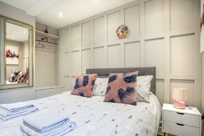 A hotel room with a bed, a bedside table, a lamp, a mirror, and a wall with a clock. - The Garden Courtyard - with free parking (York)