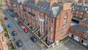 Una hilera de casas adosadas de ladrillo rojo con un patio central, una calle con coches estacionados y un cielo despejado.