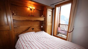 A wooden bedroom with a bed, a nightstand, a shelf with candles, and a balcony with a chair. - 50m from ski slopes, 2nd floor, view mountain, balcony, tv, 52m², La Plagne (La Plagne)