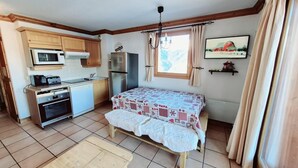 A compact room with a kitchenette, a bed with a patterned bedspread, a small table, and a window with curtains. - 50m from ski slopes, 2nd floor, view mountain, balcony, tv, 52m², La Plagne (La Plagne)