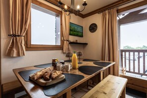 A dining area with a wooden table, black placemats, a bench, and a breakfast spread including croissants and a bottle of orange juice.