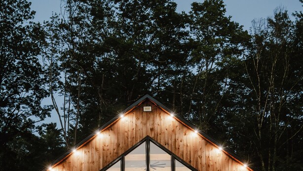 Una cabaña de madera con un gran ventanal, una terraza y una escalera que lleva a la entrada.