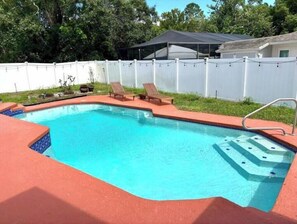 Une piscine avec une terrasse rouge, un espace abrité et une clôture blanche.