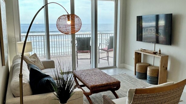 A living room with a sofa, armchairs, a coffee table, a TV, and a balcony with a view of the ocean. - Newly, renovated, modern, OCEANFRONT 2 bedroom, 2 bathroom with 25 ft balcony (Port Orange)