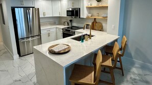 A modern kitchen with white cabinets, stainless steel appliances, a marble countertop, and a wooden island with bar stools. - Newly, renovated, modern, OCEANFRONT 2 bedroom, 2 bathroom with 25 ft balcony (Port Orange)