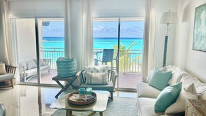 A living room with a glass coffee table, a sofa, and a chair. There is a view of the ocean through large windows.