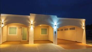 Un edificio moderno con tres ventanas iluminadas y una puerta, que presenta un techo plano y un exterior de color claro.