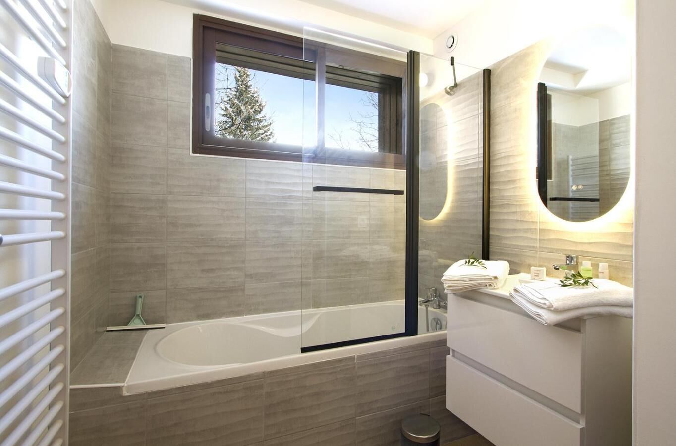A modern bathroom with a glass-enclosed shower, a large window, and a vanity with a mirror.