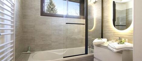 A modern bathroom with a glass-enclosed shower, a large window, and a vanity with a mirror.