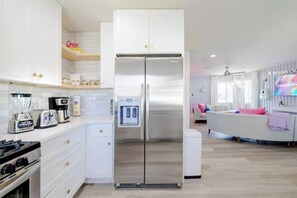 Una cocina moderna con armarios blancos, un refrigerador de acero inoxidable y una zona de comedor con una mesa y sillas blancas.