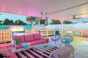 Un área de patio al aire libre con un sofá rosa, sillas azules y una mesa blanca.