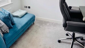 A modern bedroom with a blue sofa, a black office chair, a bookshelf, and a wall-mounted clock. - Grand 4-bed House in Ebbsfleet Valley, Garden & Parking Space (Swanscombe)