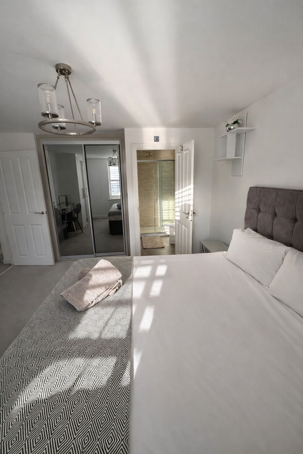 A bedroom with a large bed, a wardrobe, a mirror, and a shower area.