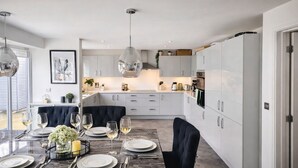 A modern kitchen with white cabinets, a dining area with a marble table, and a large pendant light. - Grand 4-bed House in Ebbsfleet Valley, Garden & Parking Space (Swanscombe)