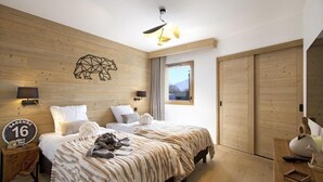 A modern hotel room with a wooden wall, a bed with a patterned blanket, a window with a view, and a sign indicating the room number.