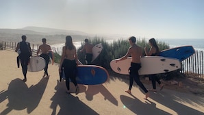 Un grupo de personas camina por un sendero costero con tablas de surf, con vistas a una playa y al océano.