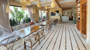 Un comedor amplio con una mesa larga, sillas de mimbre y lámparas colgantes de tejido.