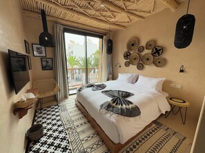 A hotel room with a large bed, a balcony with a view, a woven chair, and a patterned floor. - Palm surf&spa hotel  (Agadir)