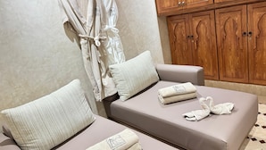 Un cuarto de spa con dos zonas de estar acolchadas, cada una con una almohada y una toalla doblada.