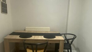 Pieni ruokailutila, jossa on puinen pöytä, kaksi tuolia, patteri ja valaisin.