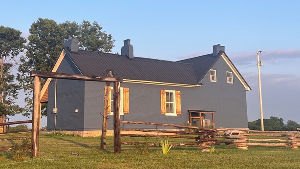 A two-story house with a dark gray exterior, a wooden porch, and a small front porch area. - Historic Farm Stay at The Hager Hideaway (Harrodsburg)